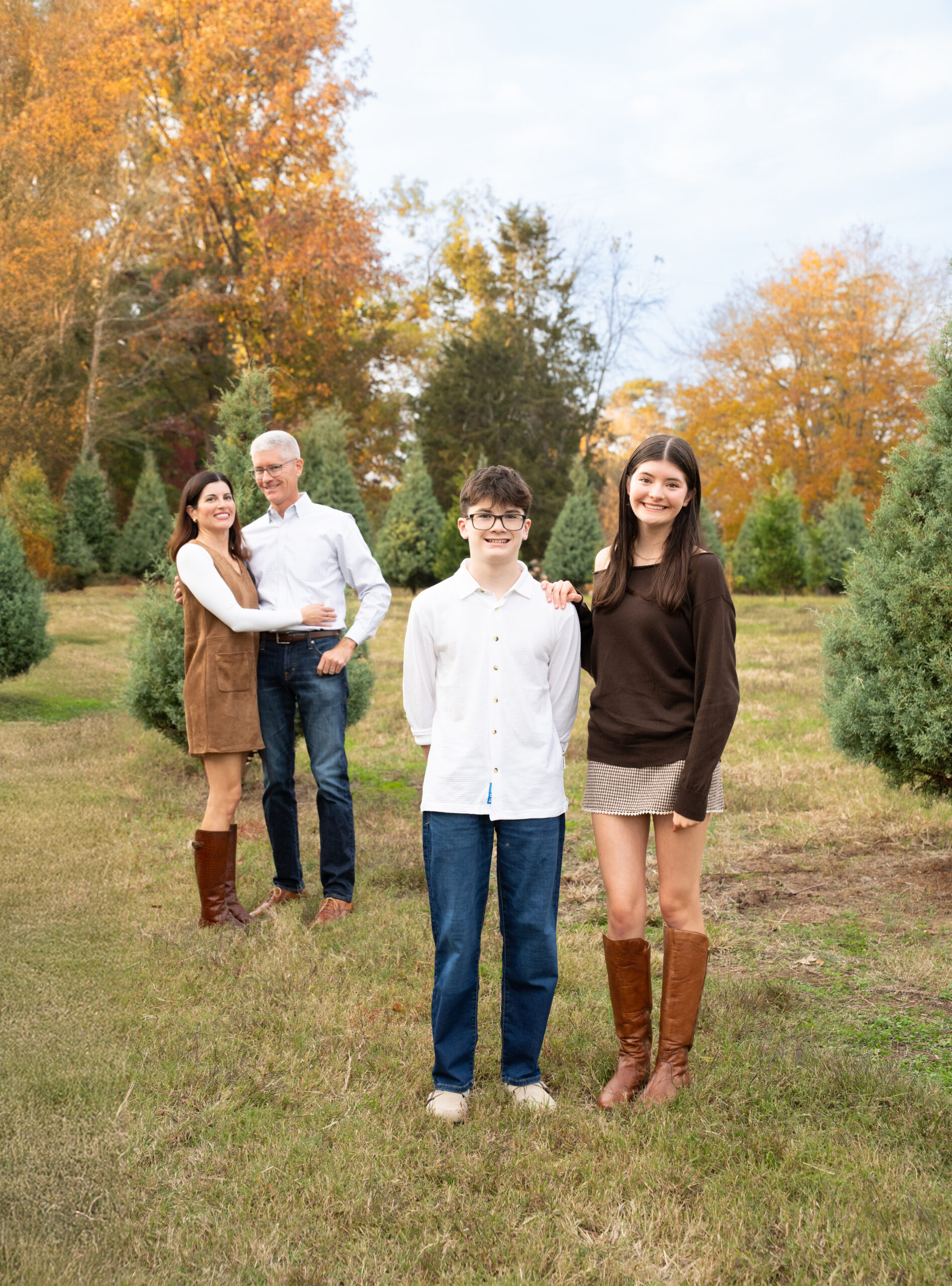 Family of four, mom, dad, brother, and sister posed on a Christmas Tree Farm during mini session by Raleigh Family Photographer