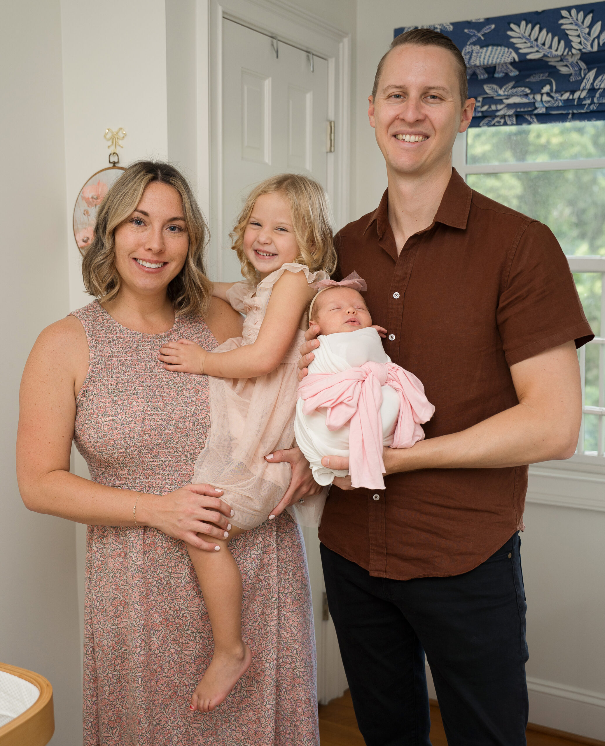 family of 4 posed with new baby in their nursery during raleigh in home newborn photography session