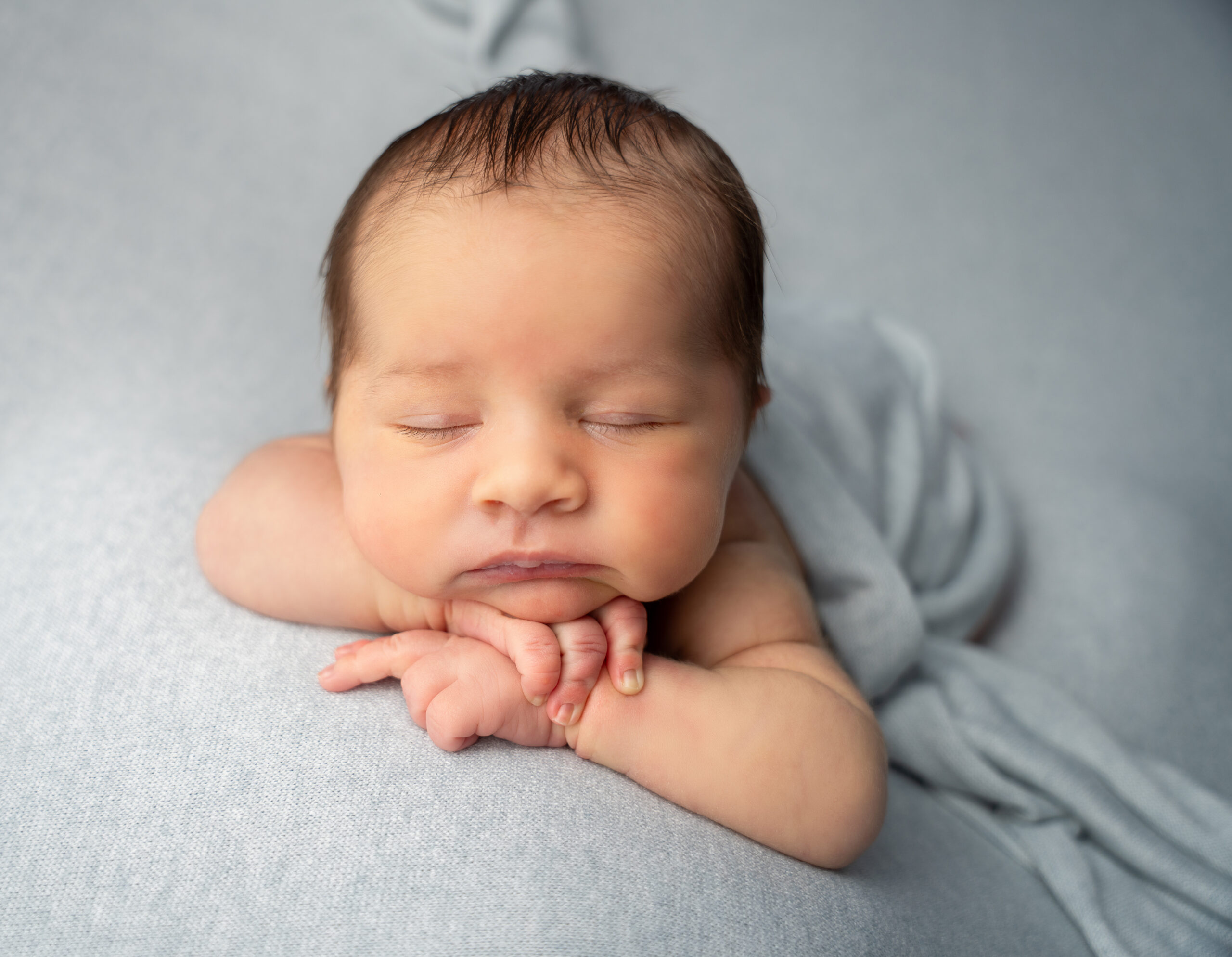 baby boy posed with chin on hands on a blue backdrop during raleigh newborn photography session