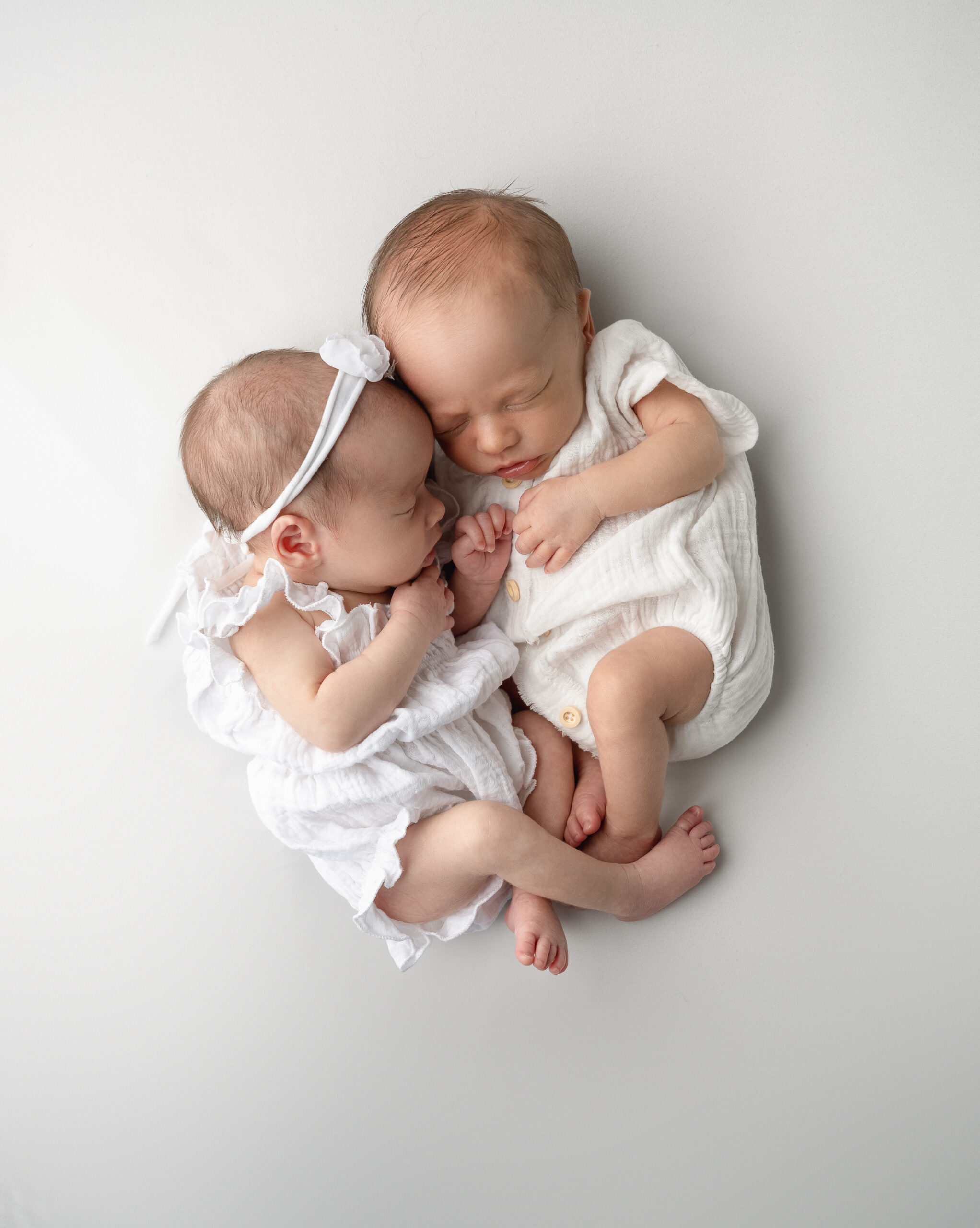 newborn boy and girl twins dressed in white outfits posed snuggled against each other during raleigh in-home newborn photography session