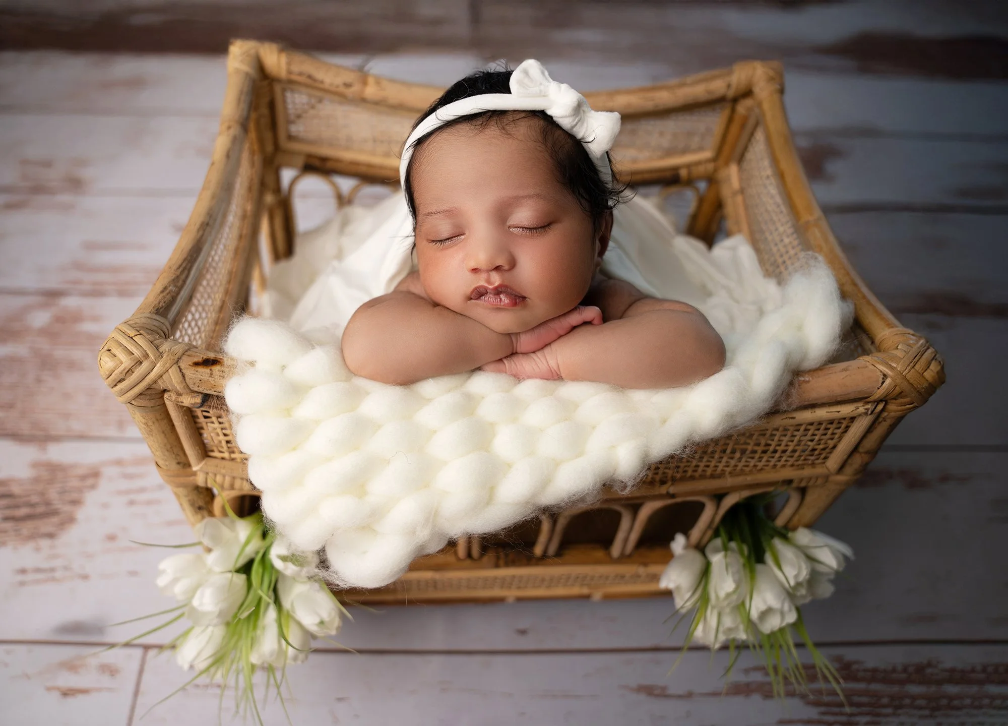 baby girl posed in a wooden crib basket with white layers and white headband